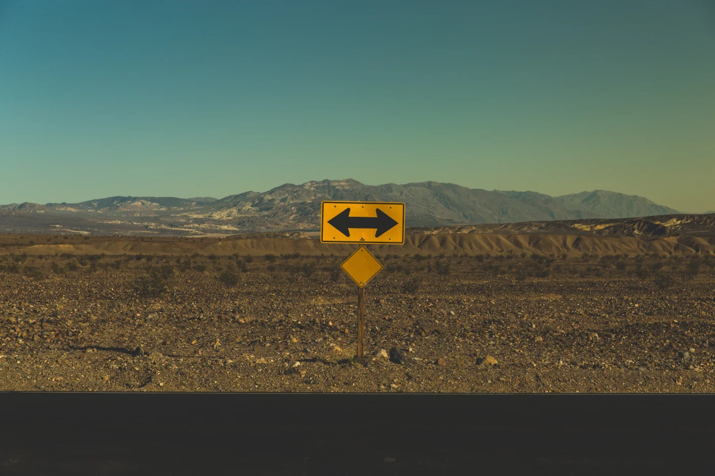 A barren rocky landscape with a roadside traffic sign depicting an arrow pointing in two opposite directions.