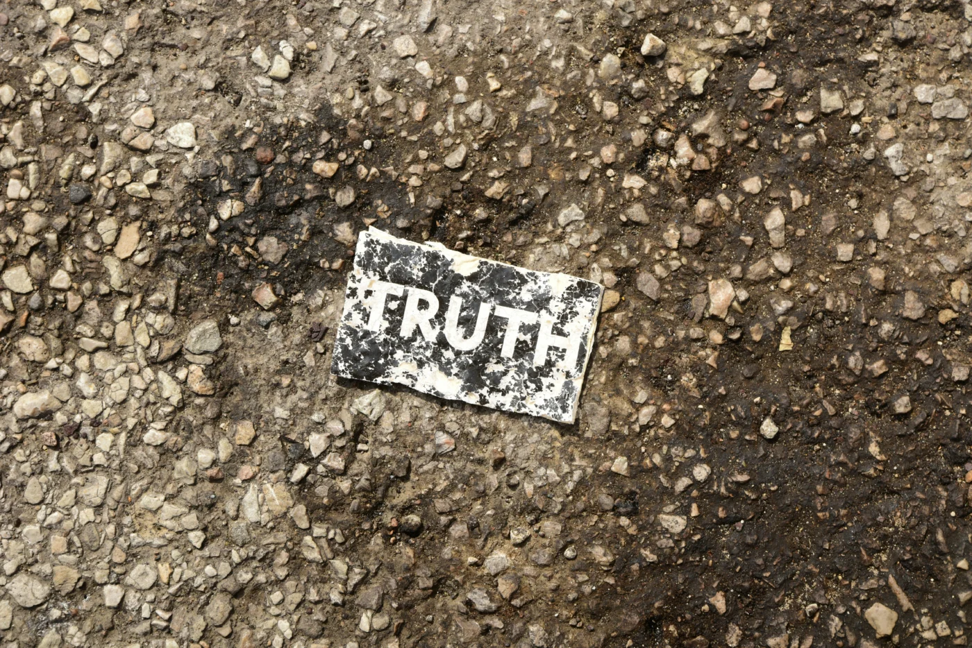 A worn and tattered black and white card bearing the word 'TRUTH' in bold type, lying on a concrete floor.
