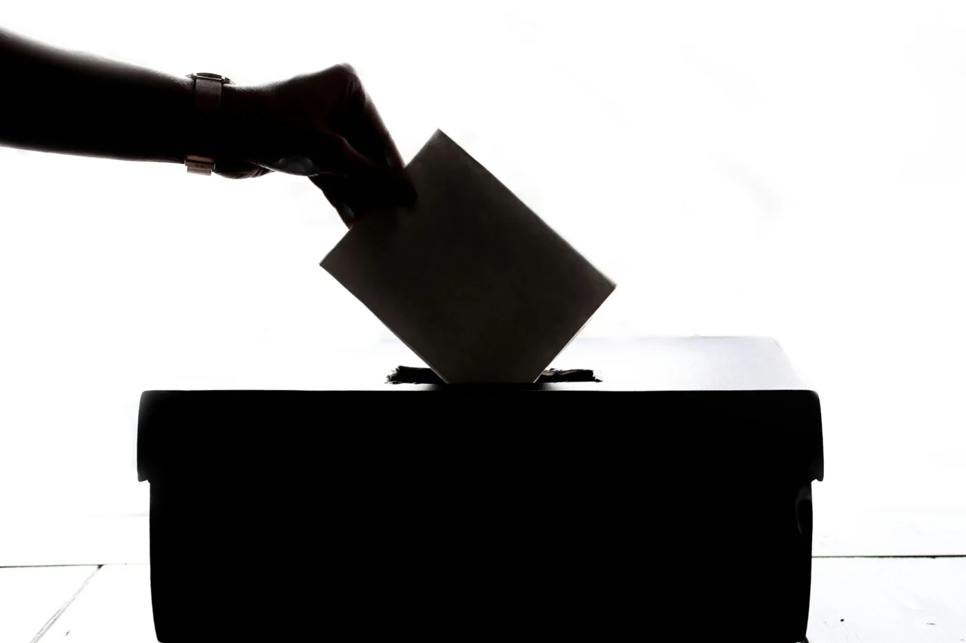 A close-up shot of someone's hand as they cast a vote into a ballot box.