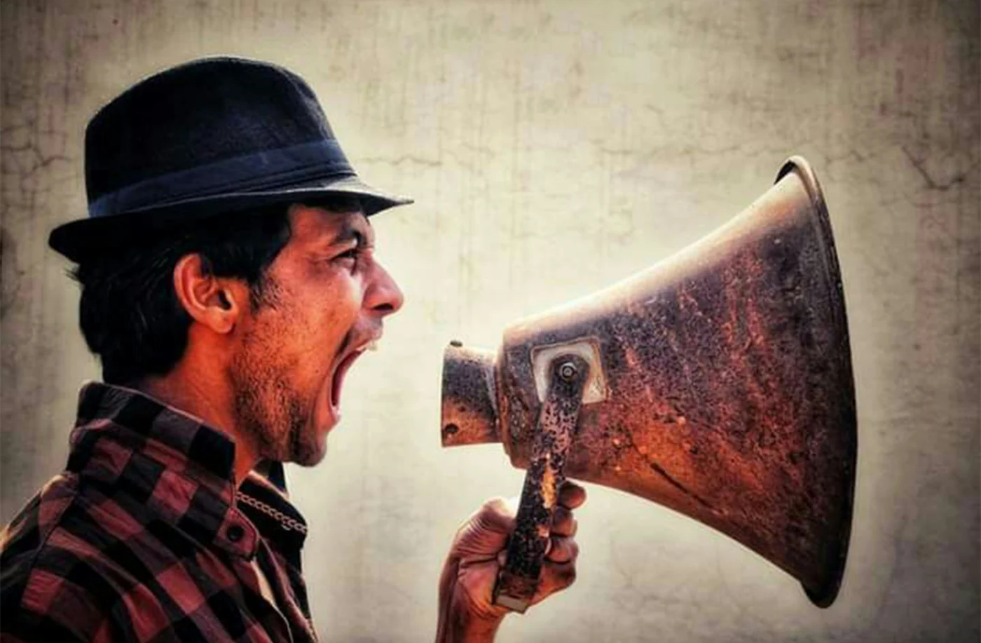 A man in a hat, shouting into a megaphone.