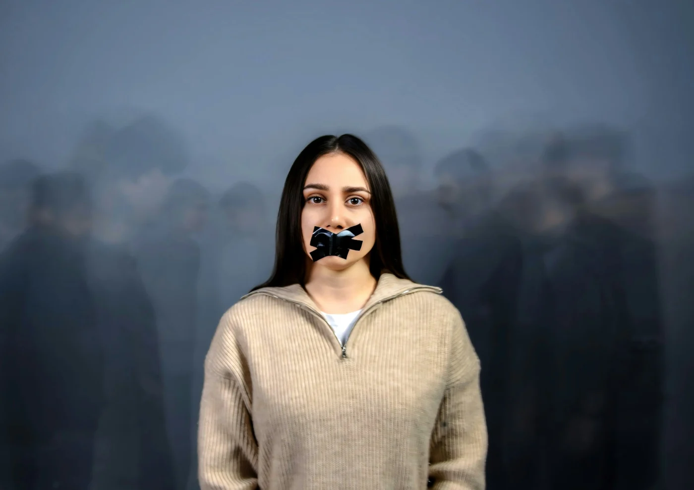 A woman with her mouth taped shut stands in front of blurred figures.