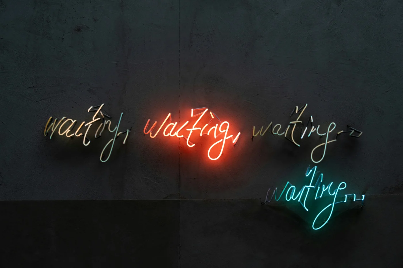 Coloured neon cursive lettering on a wall which reads "waiting, waiting, waiting, waiting..." .
